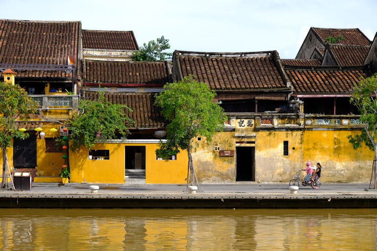 Scenic view of Hội An's historic riverside with vibrant buildings and people biking.